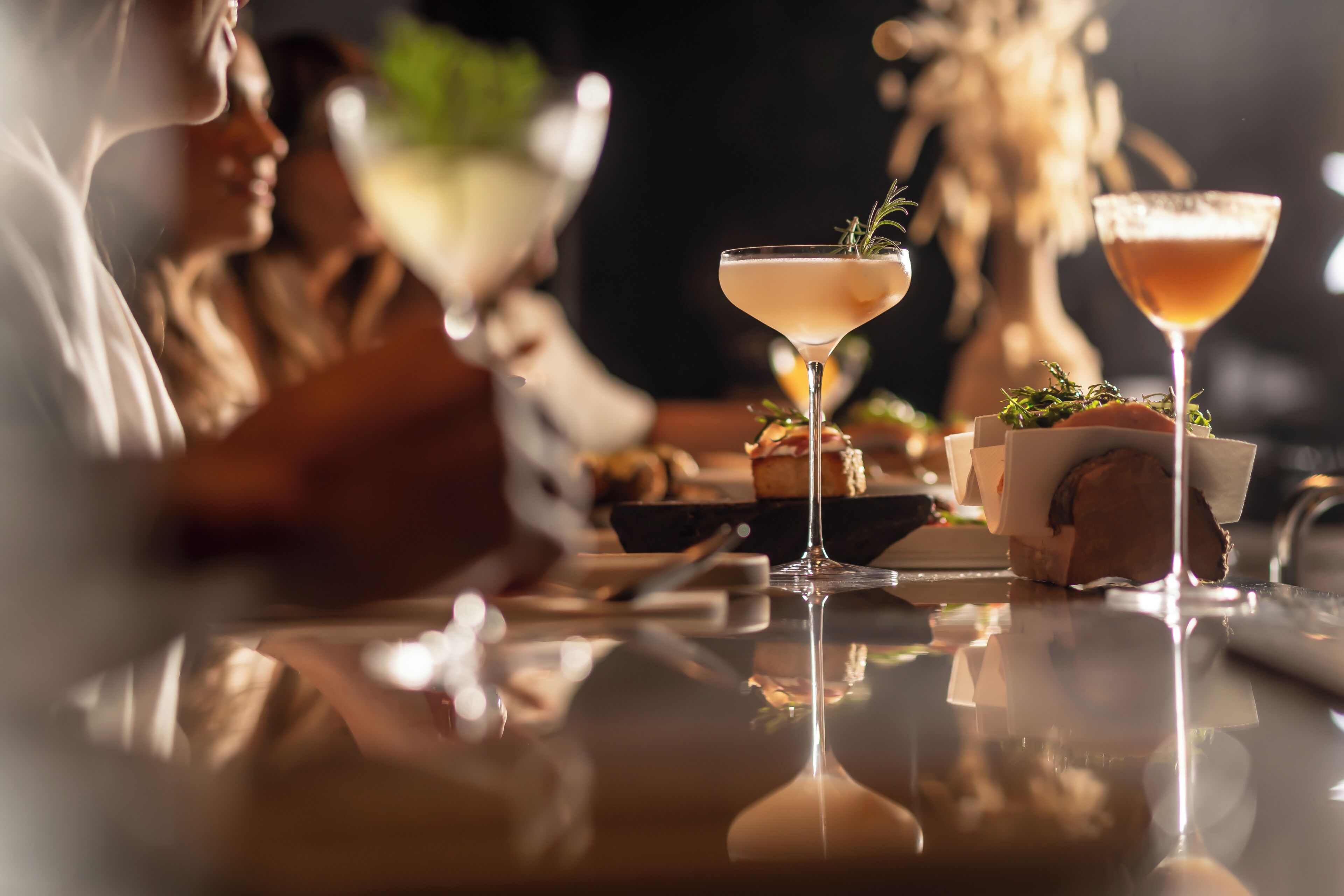 Eine Bar mit zwei Martini-Gläsern, einer Flasche und einer kleinen Schale mit Speisen.
