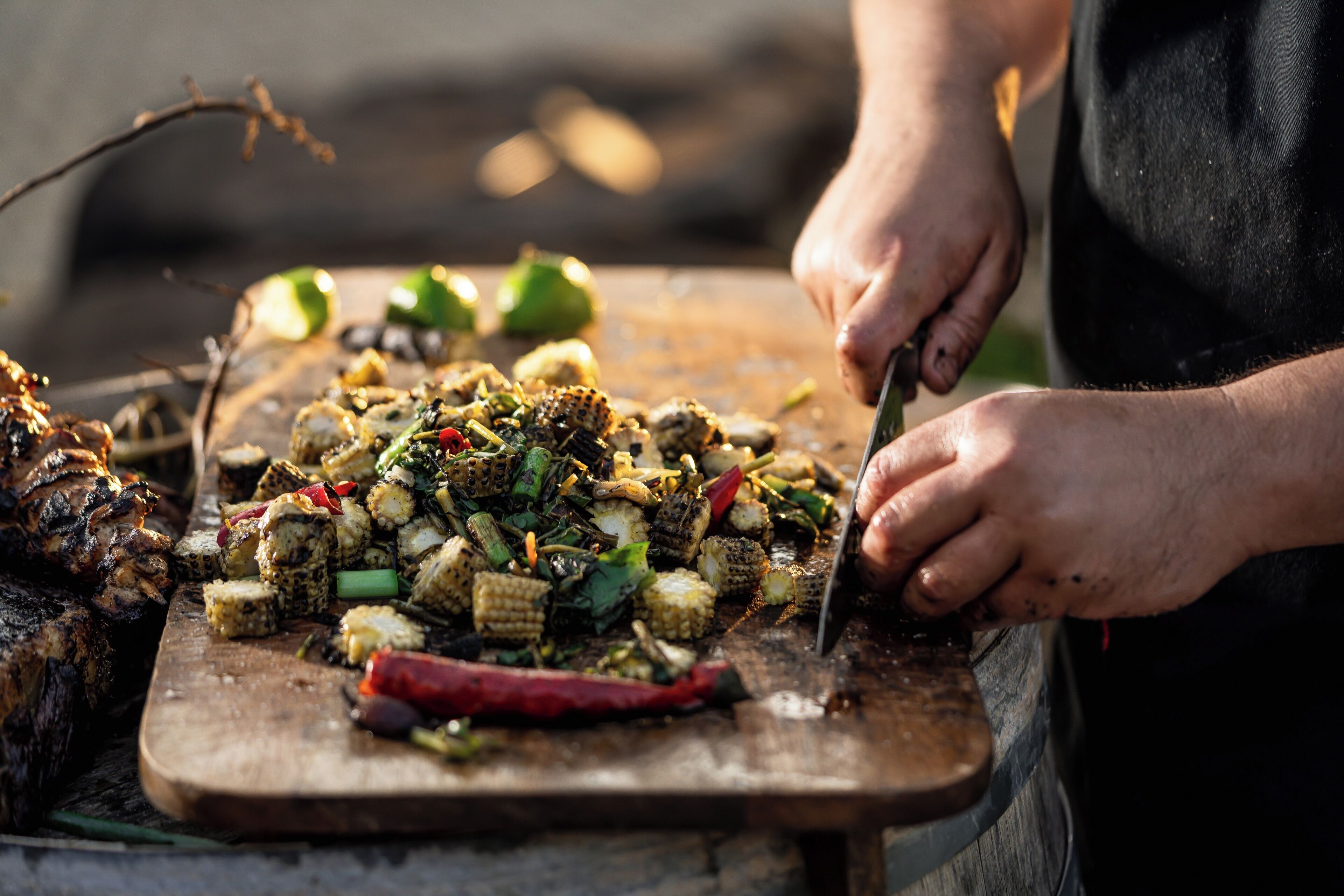 A person cutting grilled vegetables on a wooden board.