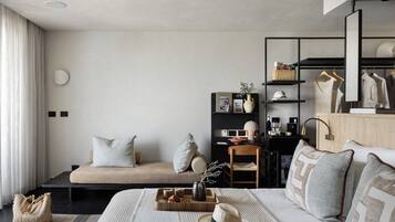 Quarto de hotel moderno com sofá, cama com almofadas decorativas, bandeja com petiscos, chapéu e espelho.