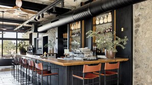 A bar area with a long counter, multiple stools, and a variety of bottles and glasses. - Pereh Mountain Resort  (Katzrin)