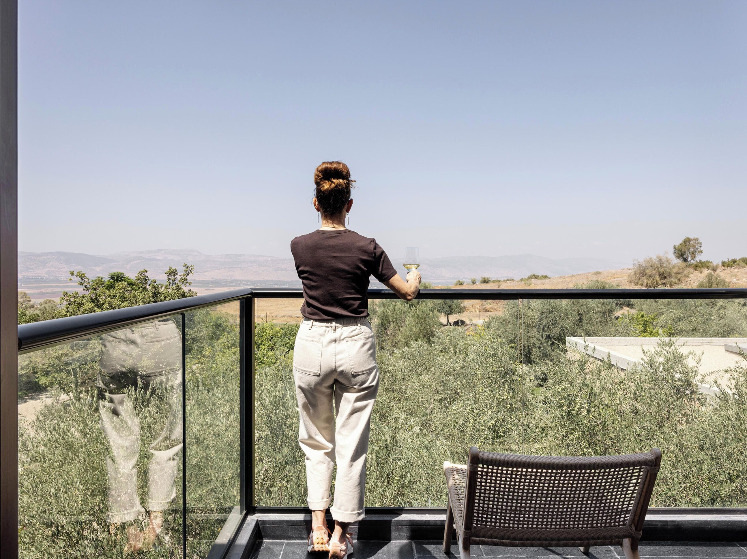 Un balcón con vistas a un paisaje, una persona de pie y una silla.