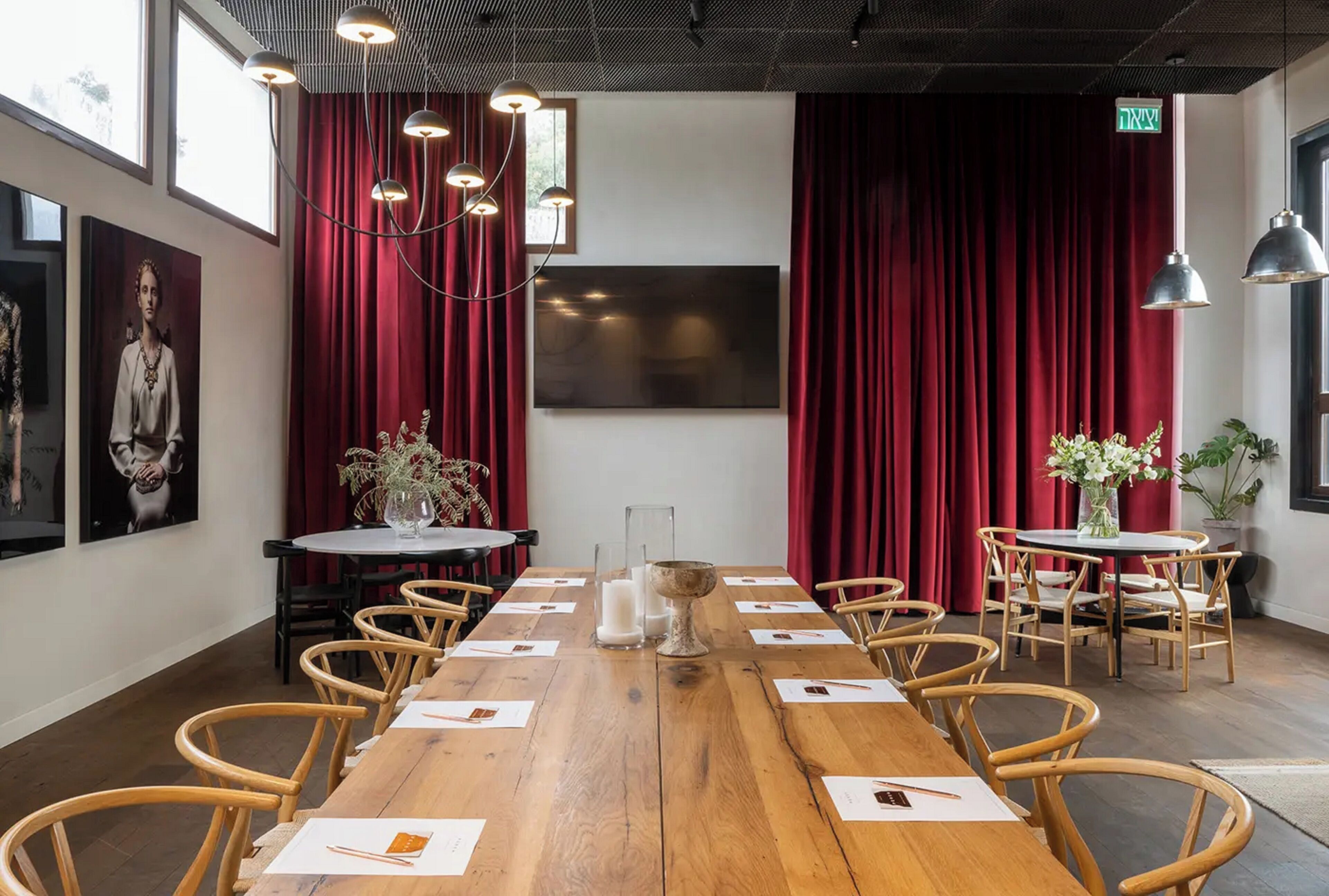 A conference room with a long wooden table, multiple chairs, a large flat-screen TV, red curtains, and pendant lighting.