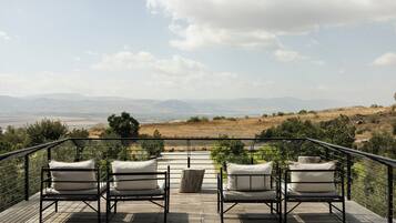 Eine Terrasse mit vier Stühlen und einem Tisch mit Blick auf eine hügelige Landschaft.