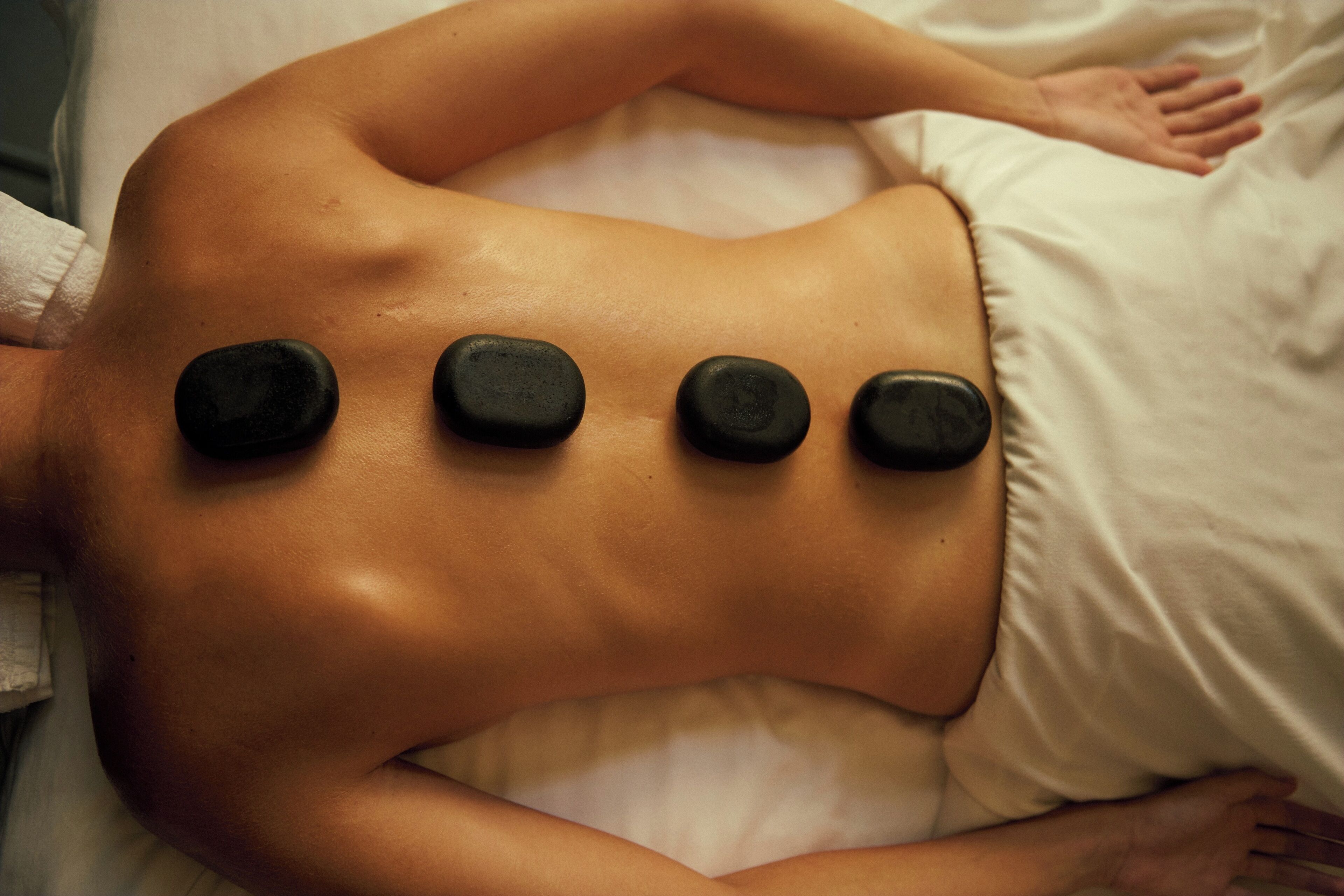 A person lying on a bed with four black stones placed on their back.