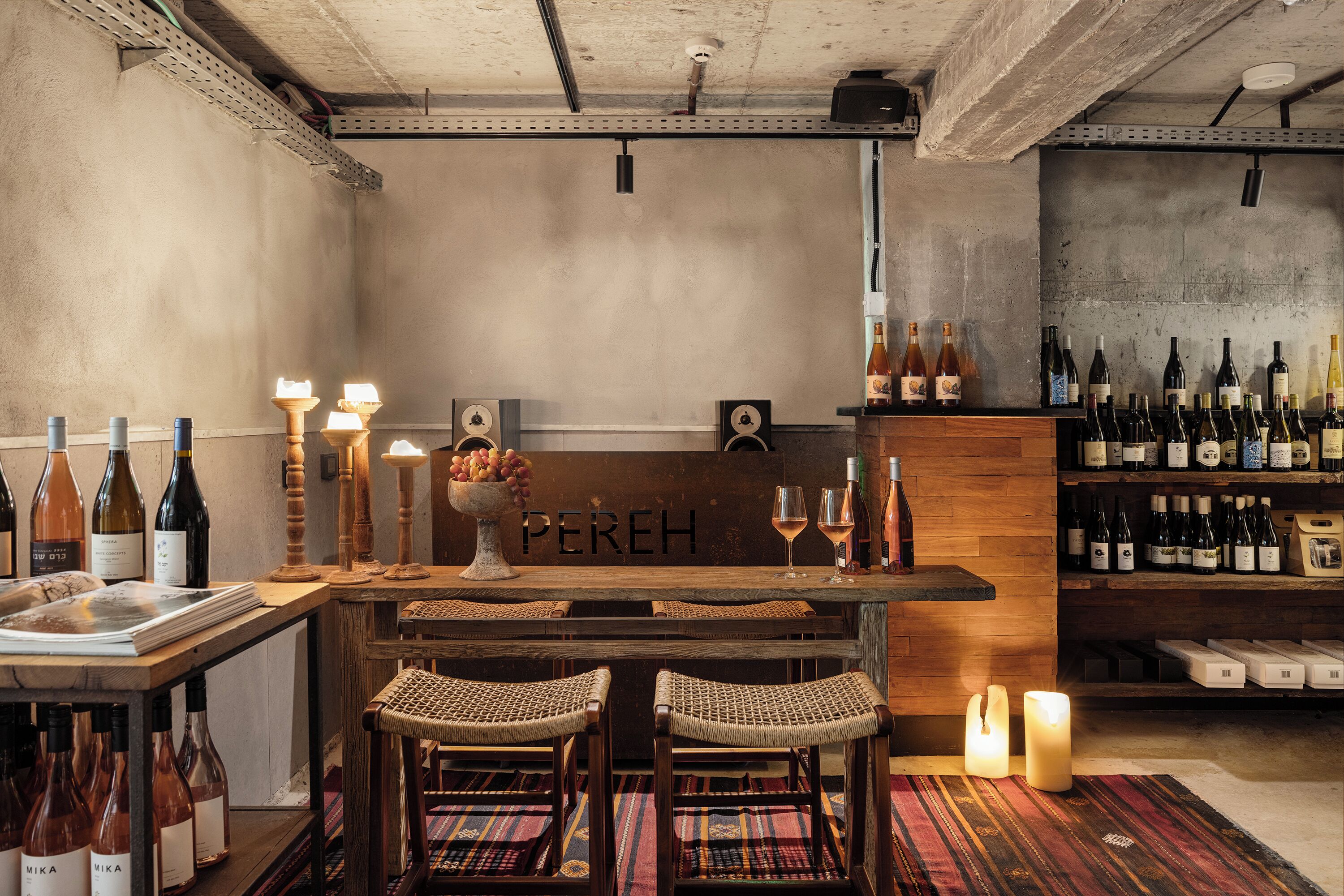 Zona de bar con mostrador de madera, taburetes, botellas de vino, copas y un letrero que dice 'PEREH'.