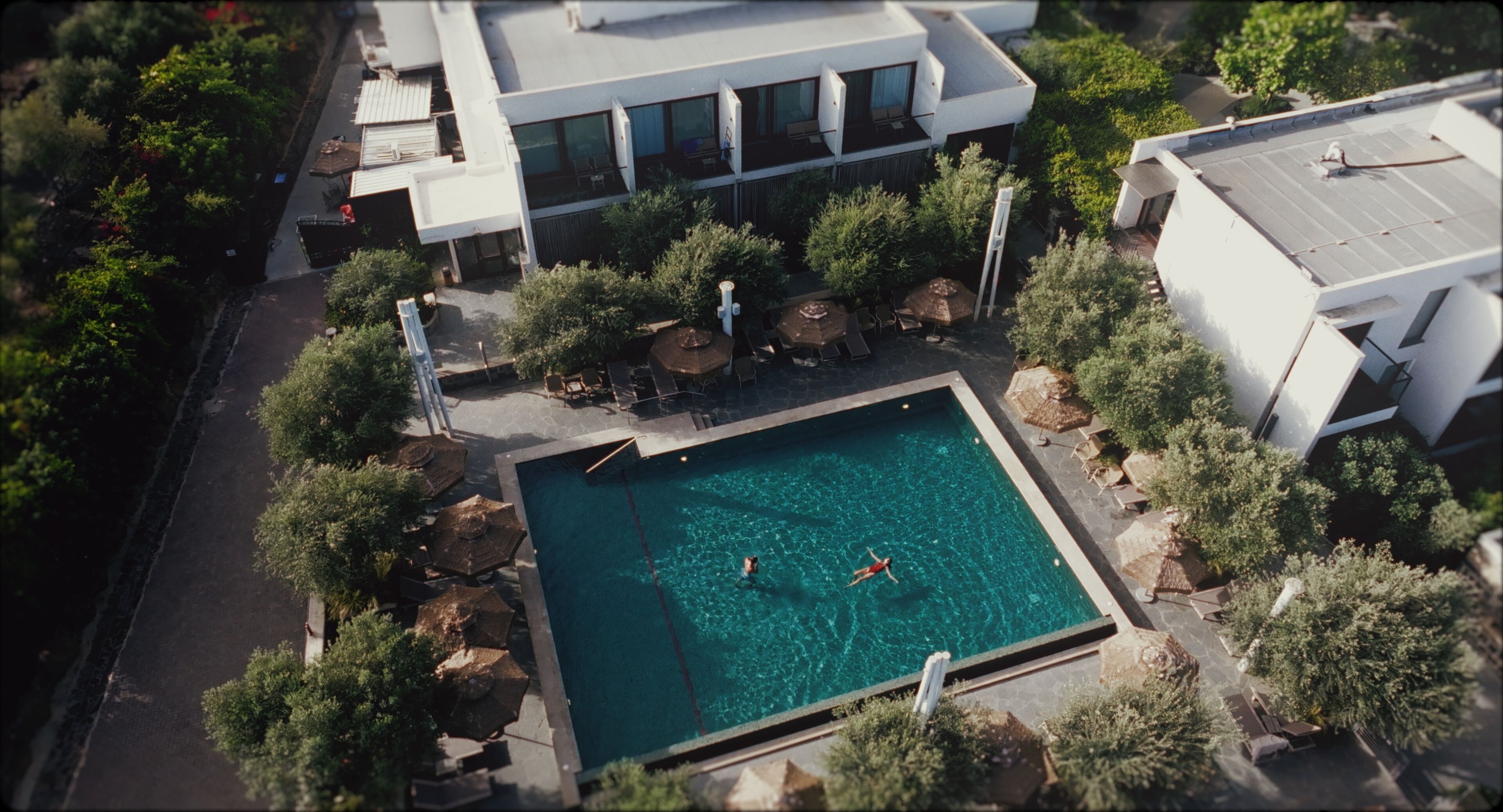 An aerial view of a modern building with a swimming pool surrounded by trees and outdoor seating.