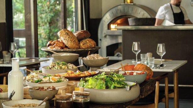 A restaurant interior with a variety of dishes, a pizza oven, and a view of greenery outside. - Pereh Mountain Resort  (Katzrin)