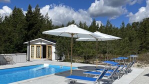 A swimming pool with blue lounge chairs and white umbrellas, surrounded by trees. - Villa Vitviken Sleeps 4 With Pool (Slite)