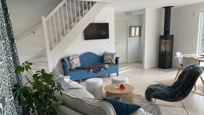 A modern living room with a blue sofa, grey armchair, and a round wooden coffee table. A staircase is visible in the background, leading to another room. - Villa Vitviken Sleeps 4 With Pool (Slite)