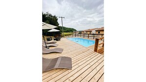 Una terraza de madera con piscina, sillas de descanso y sombrillas.
