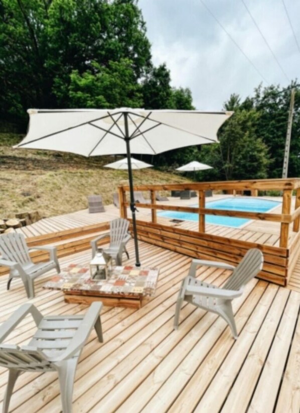 A wooden deck with outdoor seating, a pool, and umbrellas.
