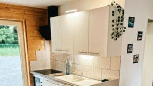Una cocina moderna con una isla central, armarios blancos y encimera negra. Hay cuatro sillas blancas alrededor de la isla.