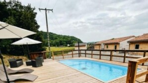 Una terraza de madera con piscina, sillas de descanso y sombrillas.