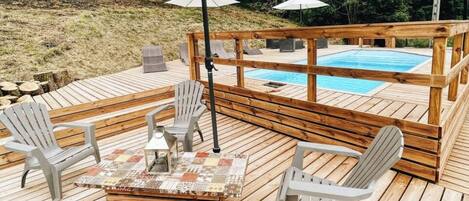 A wooden deck with a pool, outdoor seating, and umbrellas.