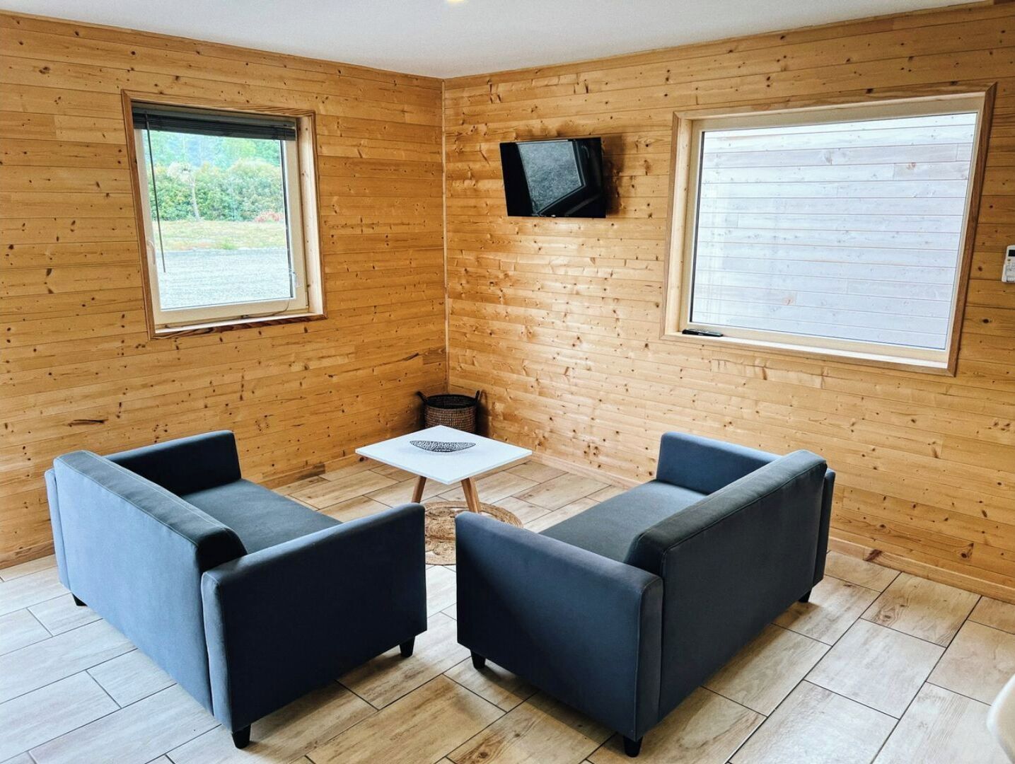 Una habitación acogedora con paredes de madera, dos sofás, una mesita y un televisor montado en la pared.