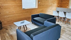 Una habitación moderna con paredes de madera, un televisor de pantalla plana, un ventanal grande y un área de estar con una mesa y sillas.
