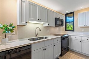 A modern kitchen with white cabinets, a stainless steel sink, a microwave, and a dishwasher. - Charming Oceanview Oasis: Wailea Elua 802 Surrounded by Lush Tropical Grounds (Wailea, Maui)