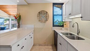 A modern kitchen with white cabinetry, a large window, and a decorative wall piece.