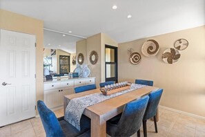 A dining area with a wooden table, blue chairs, and a decorative wall with woven patterns. - Charming Oceanview Oasis: Wailea Elua 802 Surrounded by Lush Tropical Grounds (Wailea, Maui)
