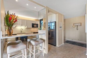 Eine moderne Küche mit weißen Schränken, einem Edelstahlkühlschrank und einer Bar mit Sitzgelegenheiten.
