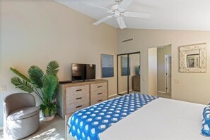 Ein Schlafzimmer mit Bett, Fernseher, Deckenventilator, Blumentopf und Spiegel.