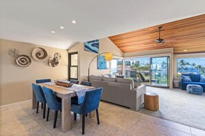 A modern living room with a dining area, a sofa, and a view of the outdoors. - Charming Oceanview Oasis: Wailea Elua 802 Surrounded by Lush Tropical Grounds (Wailea, Maui)
