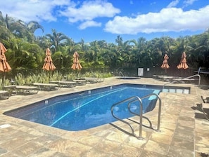Ein Swimmingpool mit Liegestühlen und Sonnenschirmen, umgeben von Palmen.