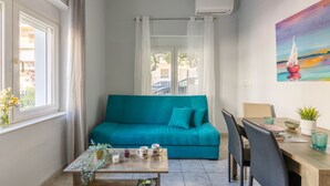 A cozy room with a teal sofa, a wooden table with drinks and a magazine, and a painting of a sailboat on the wall. - Klio's cozy house city center (Heraklion)