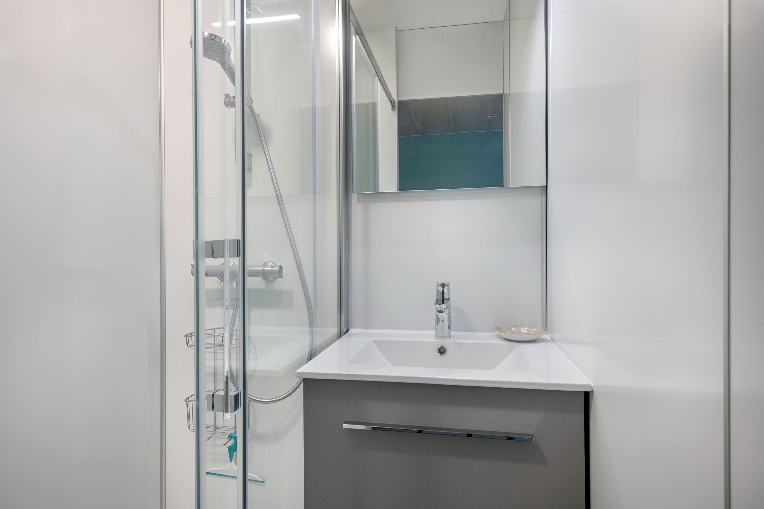 Un bagno moderno con box doccia in vetro, un lavandino bianco e uno specchio sopra al lavandino.