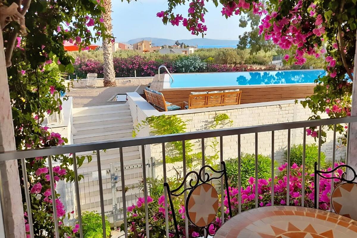 A balcony with a view of a swimming pool, surrounded by pink flowers and a wooden deck.