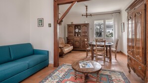 Un salón con un sofá azul, una mesa de comedor de madera, sillas, un tapete estampado y un armario de madera.