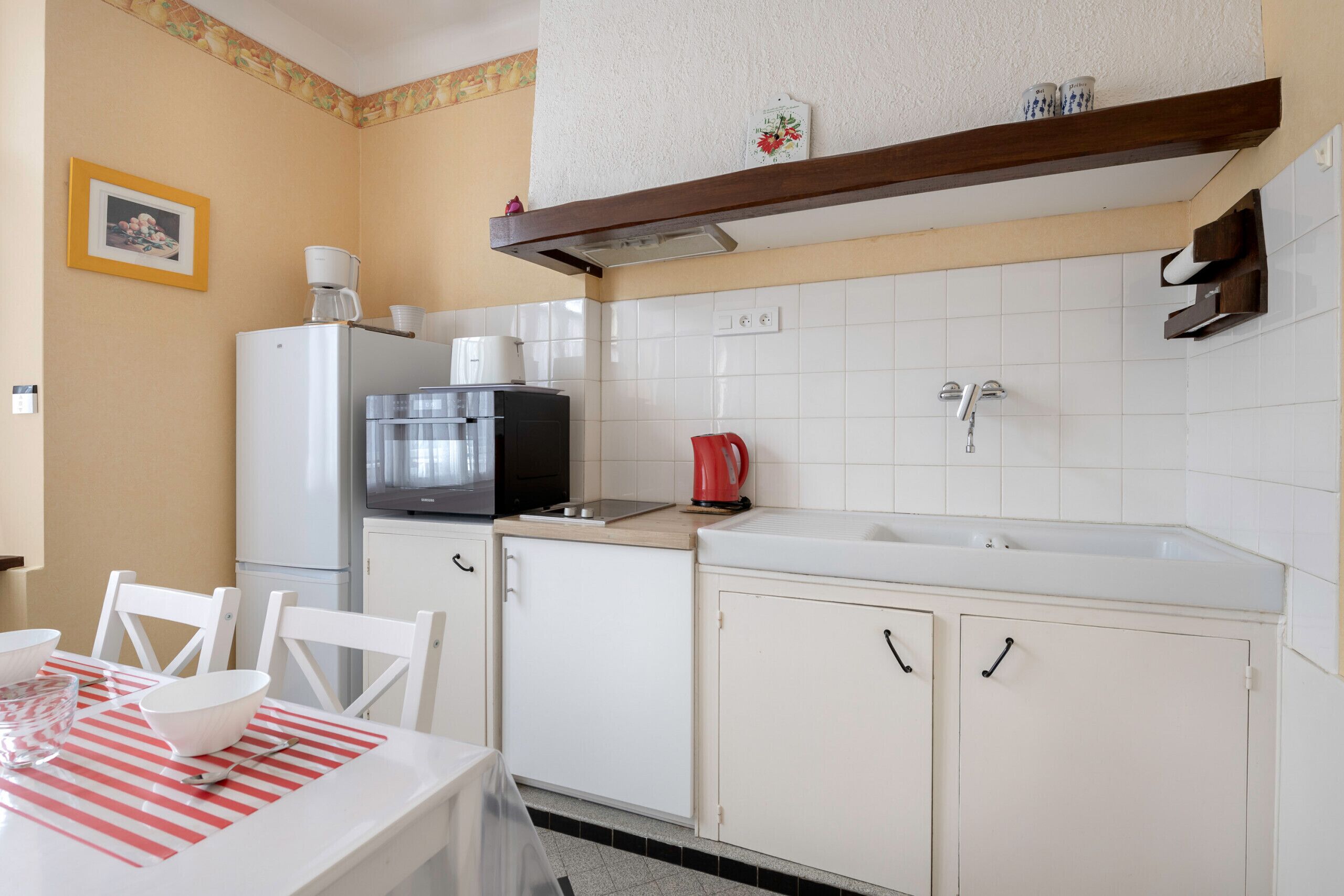 A compact kitchen with white cabinets, a refrigerator, a coffee maker, and a sink.