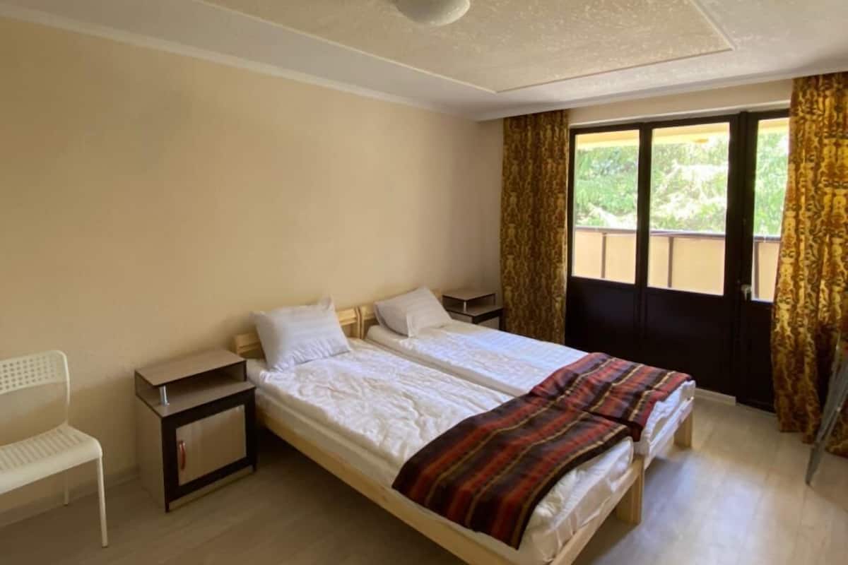 A bedroom with a large bed, a nightstand, a chair, and a window with curtains.