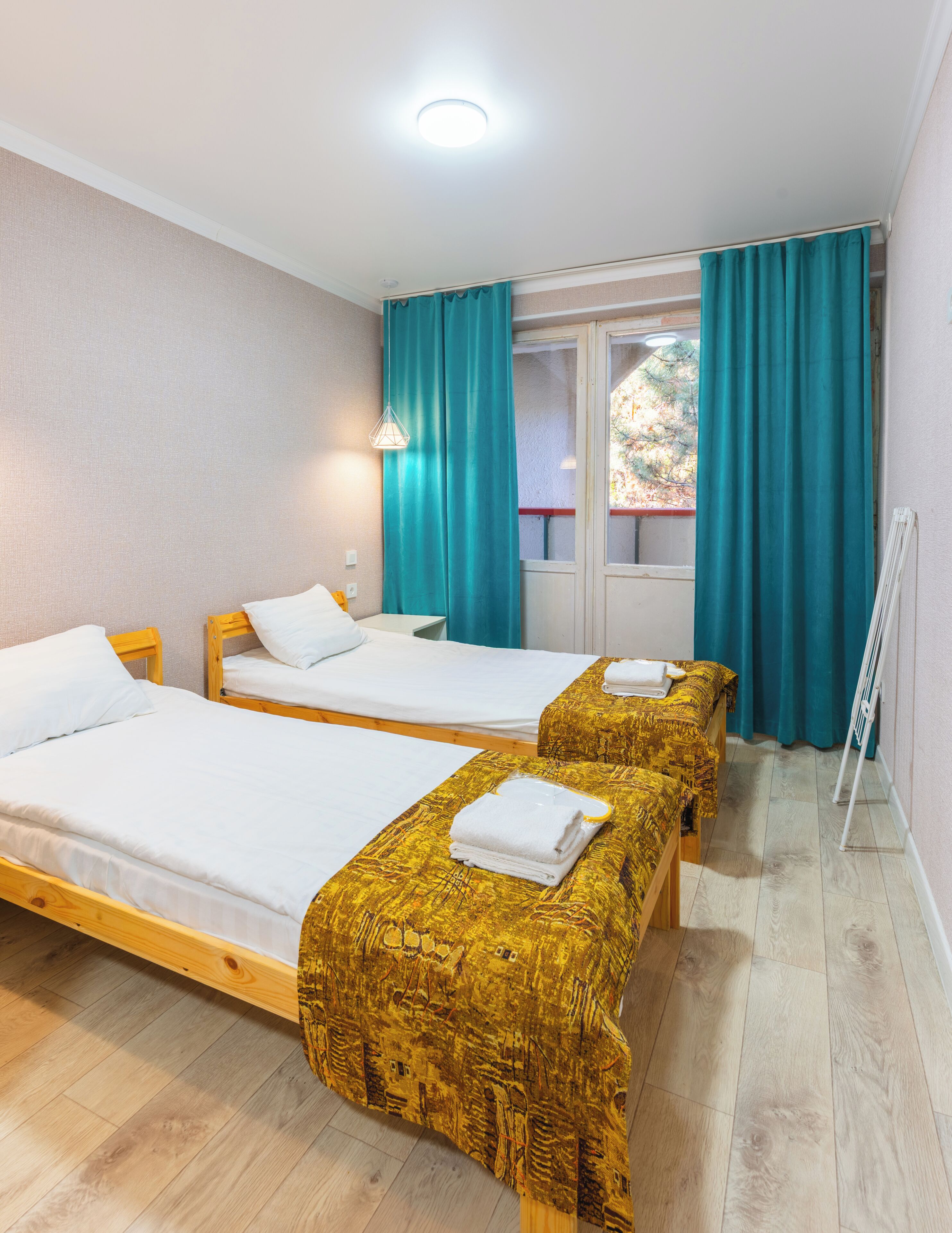 A room with two beds, a window with curtains, a radiator, and a wooden floor.