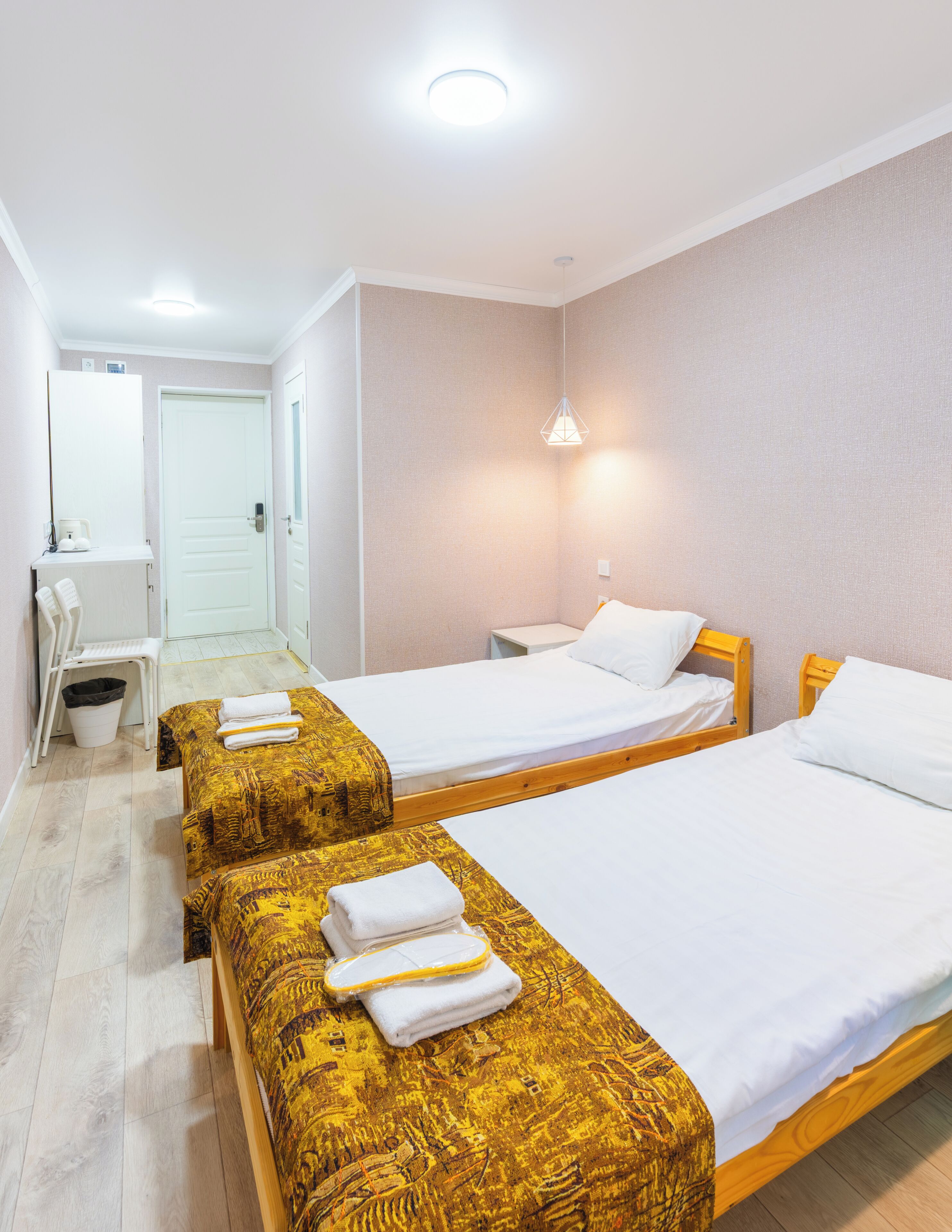 A hotel room with two beds, a desk, a chair, and a small bathroom.