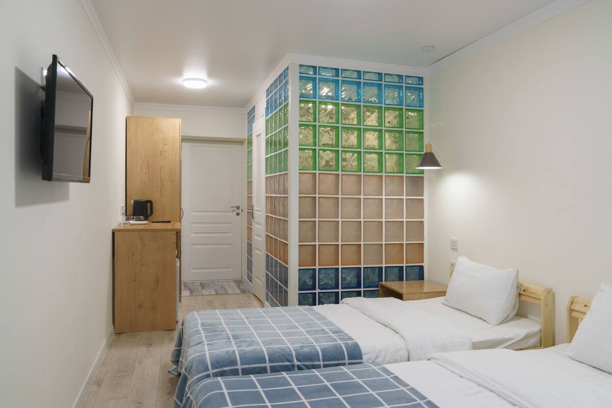 A bedroom with two beds, a wooden wardrobe, a mirror, and a wall with a grid pattern.