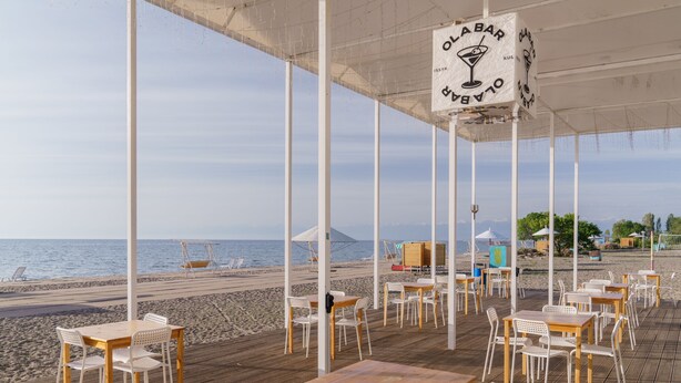 Um restaurante à beira-mar com mesas e cadeiras brancas ao ar livre, com vista para o mar.
