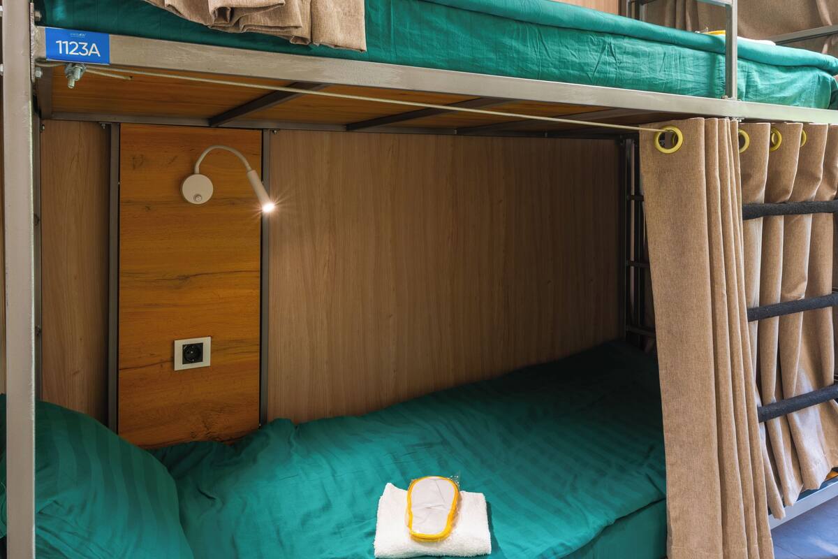 A bunk bed with a green mattress, a wooden door, and a towel on the lower bunk.