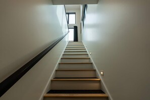 A modern staircase with wooden steps and a black handrail, leading to a bright room with a window.