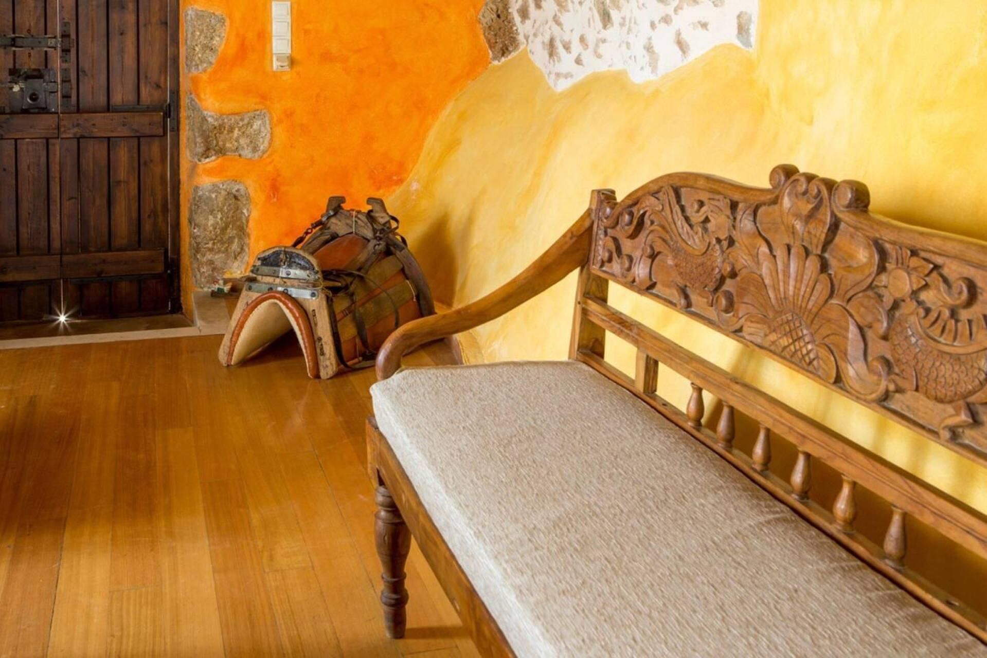 A wooden bench with a cushioned seat and backrest, a rustic wall with exposed stone, and a wooden door with a metal latch.