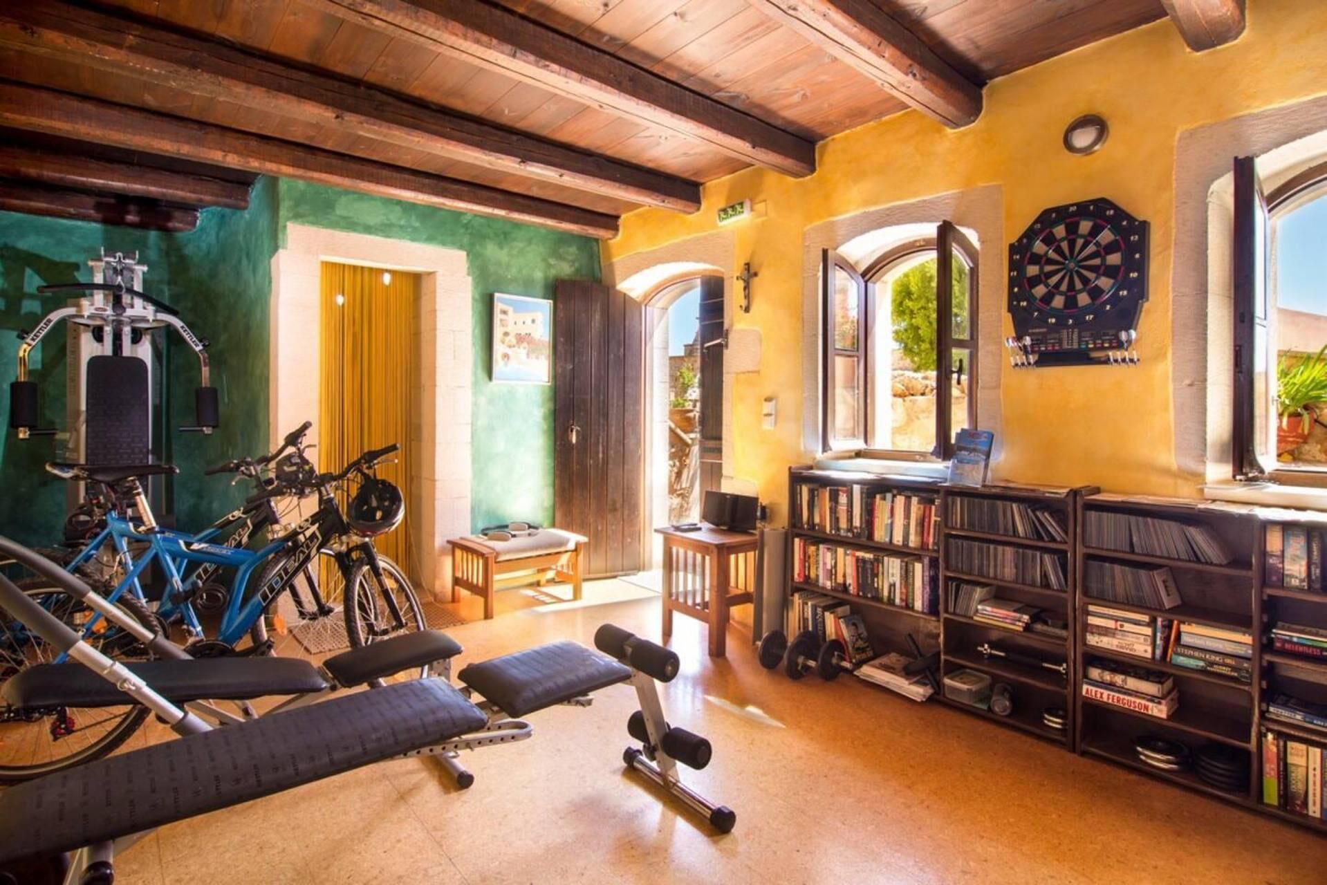 Een sportschool aan huis met fitnessapparatuur, een boekenkast en een dartbord.