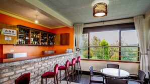 A bar area with a brick wall, red bar stools, and a round table with wicker chairs. - THE CRESTED CRANE BWINDI HOTEL (Kyesero)
