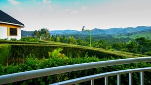 A house with a white exterior and yellow trim, surrounded by lush greenery and mountains in the background. - THE CRESTED CRANE BWINDI HOTEL (Kyesero)
