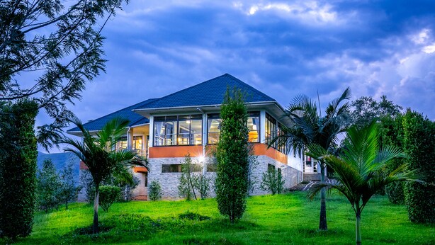 A modern house with a large glass window, surrounded by lush greenery and a blue sky. - THE CRESTED CRANE BWINDI HOTEL (Kyesero)