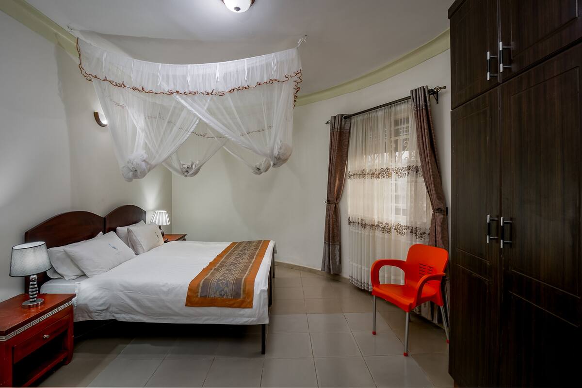 A bedroom with a bed, bedside table, lamp, wardrobe, and a chair.