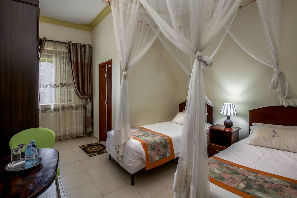 A hotel room with a bed, a nightstand, a table with water bottles, and a chair.