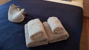 Un lit bien fait, avec des oreillers et une couverture bleue, un petit sac en tissu tressé et des serviettes enroulées posées sur le lit.