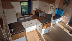Une cuisine compacte avec des meubles blancs, un évier, un four à micro-ondes et une fenêtre donnant sur un espace verdoyant.