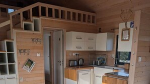 Une cuisine compacte équipée d’un évier, d’une cuisinière et de placards, un coin repas avec une table et des chaises, et un escalier menant à un niveau supérieur.