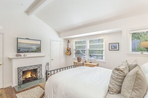 Quarto com lareira, uma cama, um violão e uma janela com persianas.